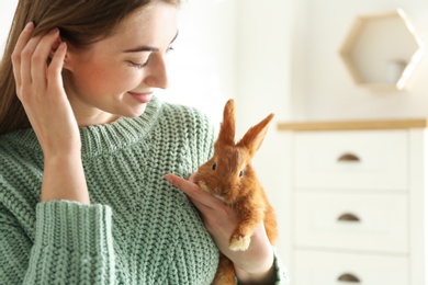 Photo of Young woman with adorable rabbit indoors. Lovely pet