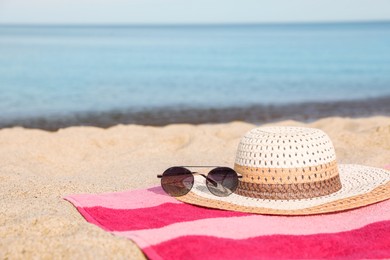 Photo of Beach towel with straw hat and sunglasses on sand near sea. Space for text
