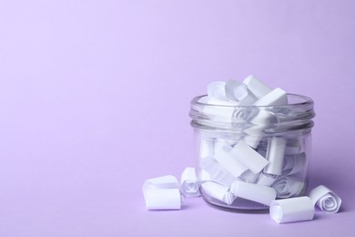Photo of Glass jar full of rolled paper sheets on violet background, space for text
