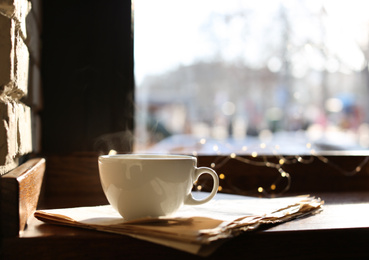 Photo of Delicious morning coffee and newspaper near window, indoors