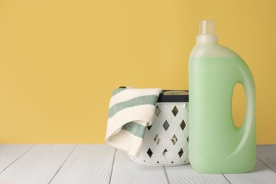 Photo of Bottle of fabric softener and towels in basket on white wooden table, space for text