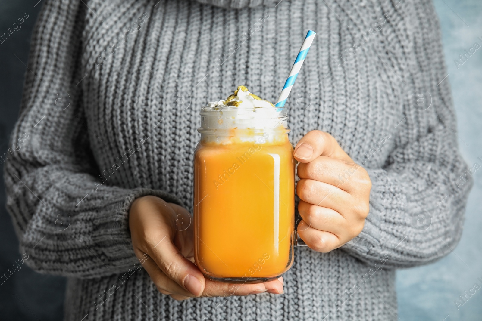 Photo of Woman in knitted sweater holding mason jar with pumpkin spice latte and whipped cream, closeup