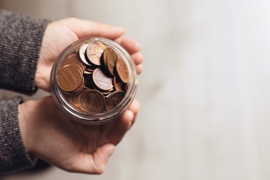 Woman holding donation jar with coins on light background, top view. Space for text