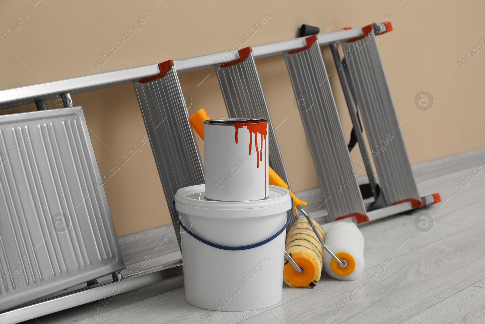 Photo of Metallic folding ladder and painting tools near beige wall indoors