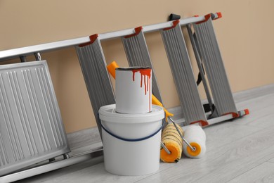 Metallic folding ladder and painting tools near beige wall indoors