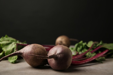 Photo of Fresh beets with leaves on grey table against black background, closeup. Space for text