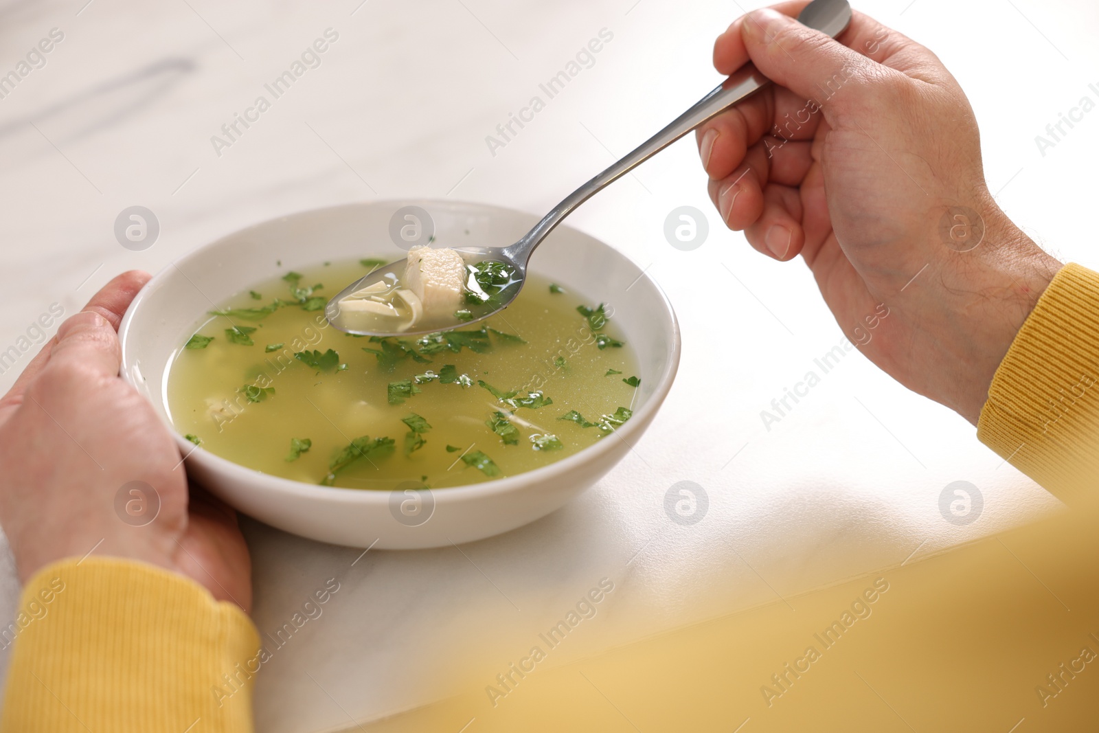 Photo of Man eating delicious chicken soup at light table, closeup