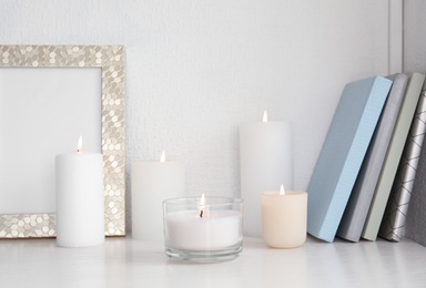 Burning aromatic candles in holders on bookshelf