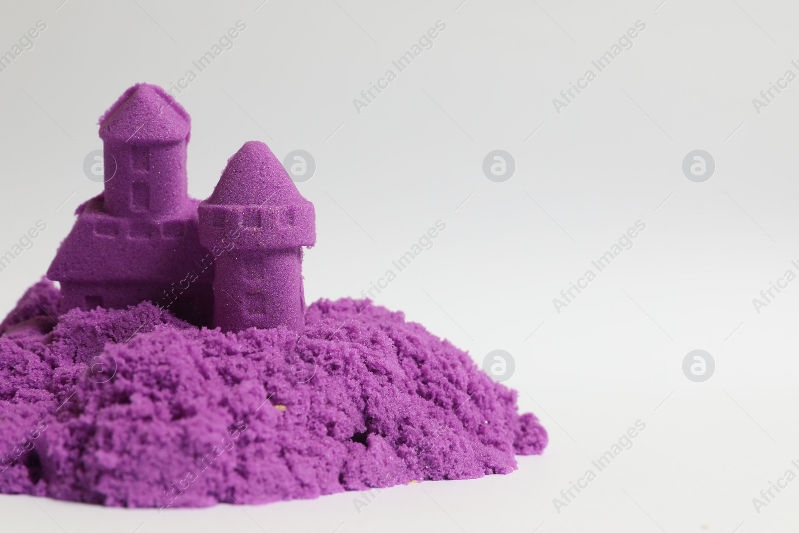 Photo of Castle made of purple kinetic sand on white background. Space for text