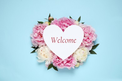 Image of Welcome card in shape of heart and beautiful peonies on light blue background, top view