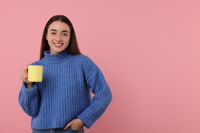 Photo of Happy young woman holding yellow ceramic mug on pink background, space for text