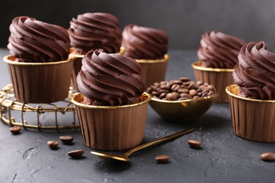 Photo of Delicious chocolate cupcakes and coffee beans on black textured table
