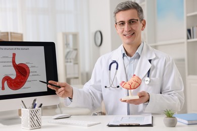Photo of Gastroenterologist with human model showing screen with illustration of stomach at table in clinic