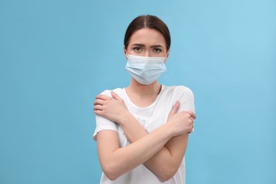 Photo of Woman in mask suffering from fever on light blue background. Cold symptoms