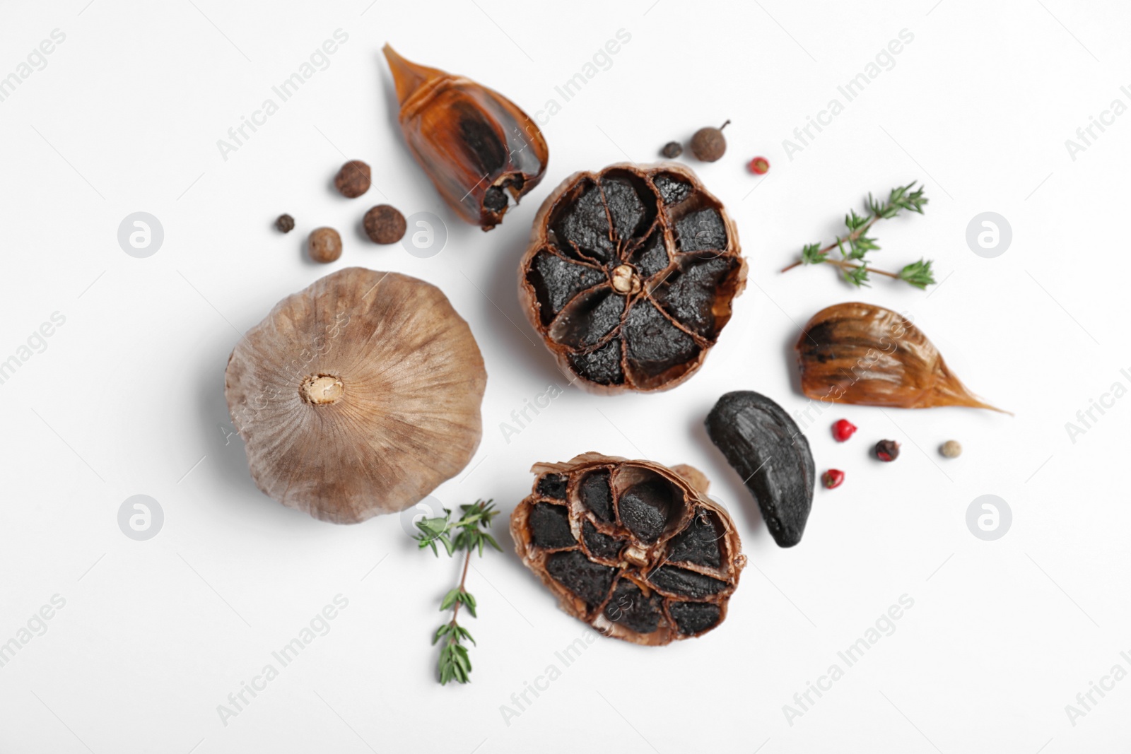 Photo of Aged black garlic with thyme and peppercorns on white background, view from above