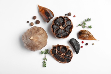 Photo of Aged black garlic with thyme and peppercorns on white background, view from above