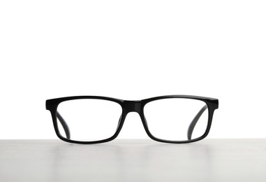 Stylish glasses with black frame on table against white background