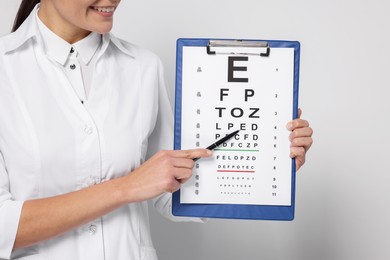 Photo of Ophthalmologist pointing at vision test chart on light background, closeup