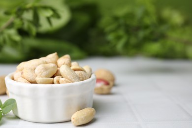 Photo of Fresh peeled peanuts in bowl on white tiled table against blurred green background, closeup. Space for text