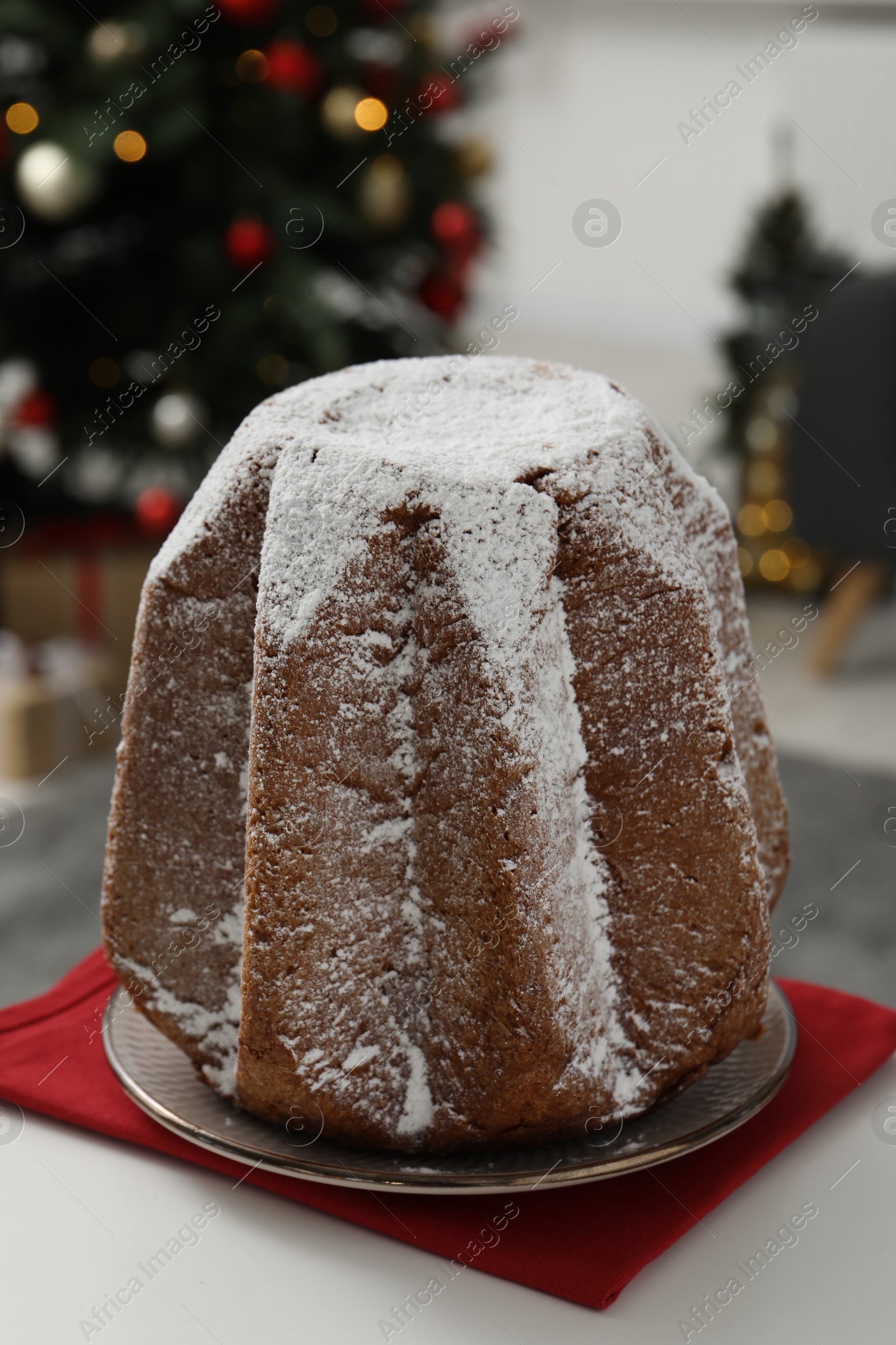 Photo of Traditional Italian pastry. Delicious Pandoro cake decorated with powdered sugar on white table in room