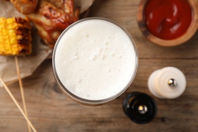 Photo of Glass of beer, delicious baked chicken wings, grilled corn and sauce on wooden table, closeup