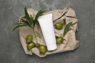 Photo of Tube of cream with olive essential oil and kraft crumpled paper on dark grey table, top view