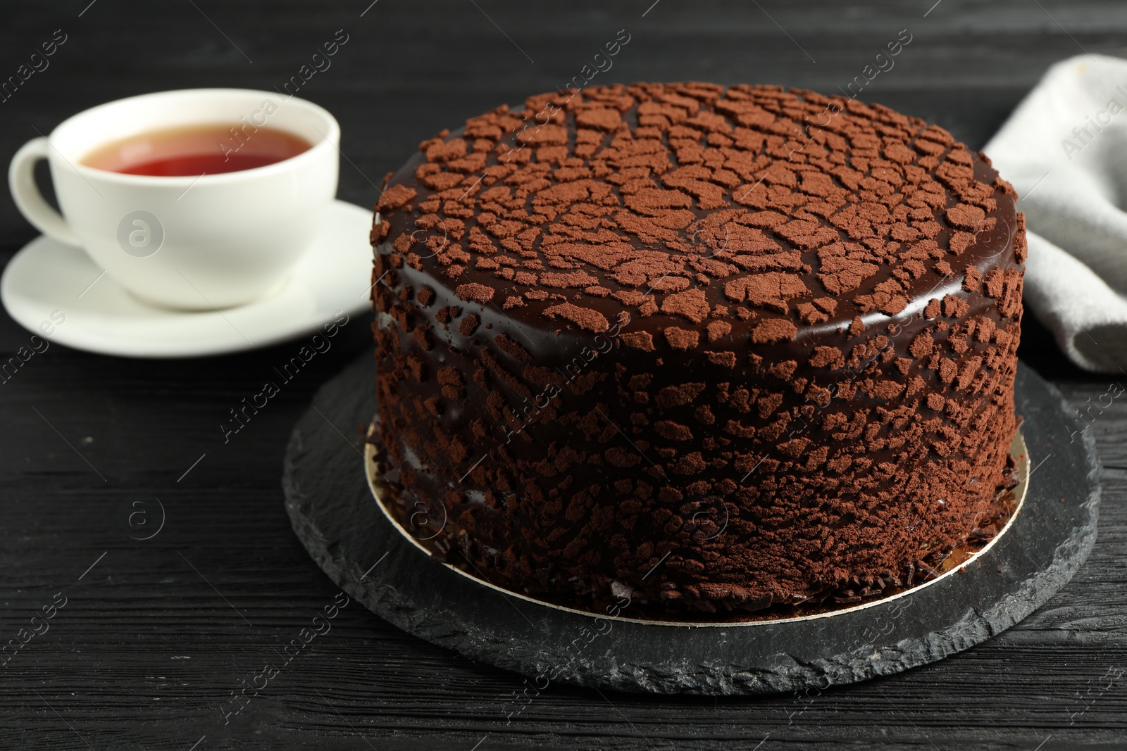 Photo of Delicious chocolate truffle cake and tea on black wooden table