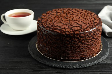 Photo of Delicious chocolate truffle cake and tea on black wooden table