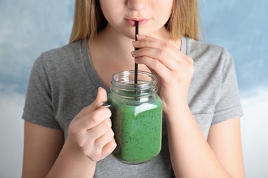 Woman drinking spirulina smoothie from mason jar on color background, closeup