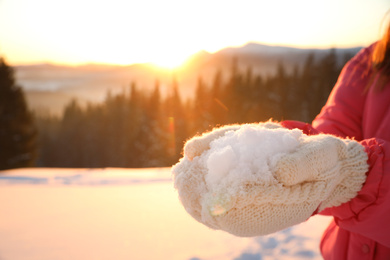 Photo of Woman holding pile of snow outdoors, closeup view with space for text. Winter vacation