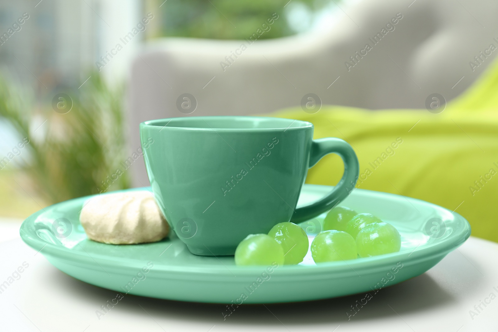 Photo of Green cup and plate with mint candies on table against blurred background