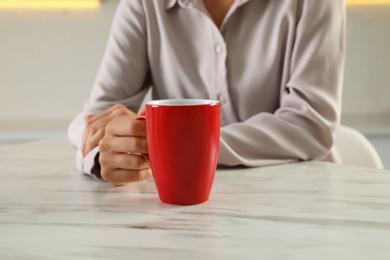 Photo of Woman with red cup at table indoors, closeup