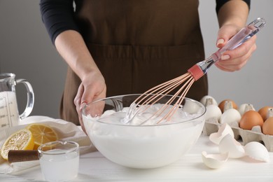 Woman making whipped cream with whisk at white wooden table, closeup