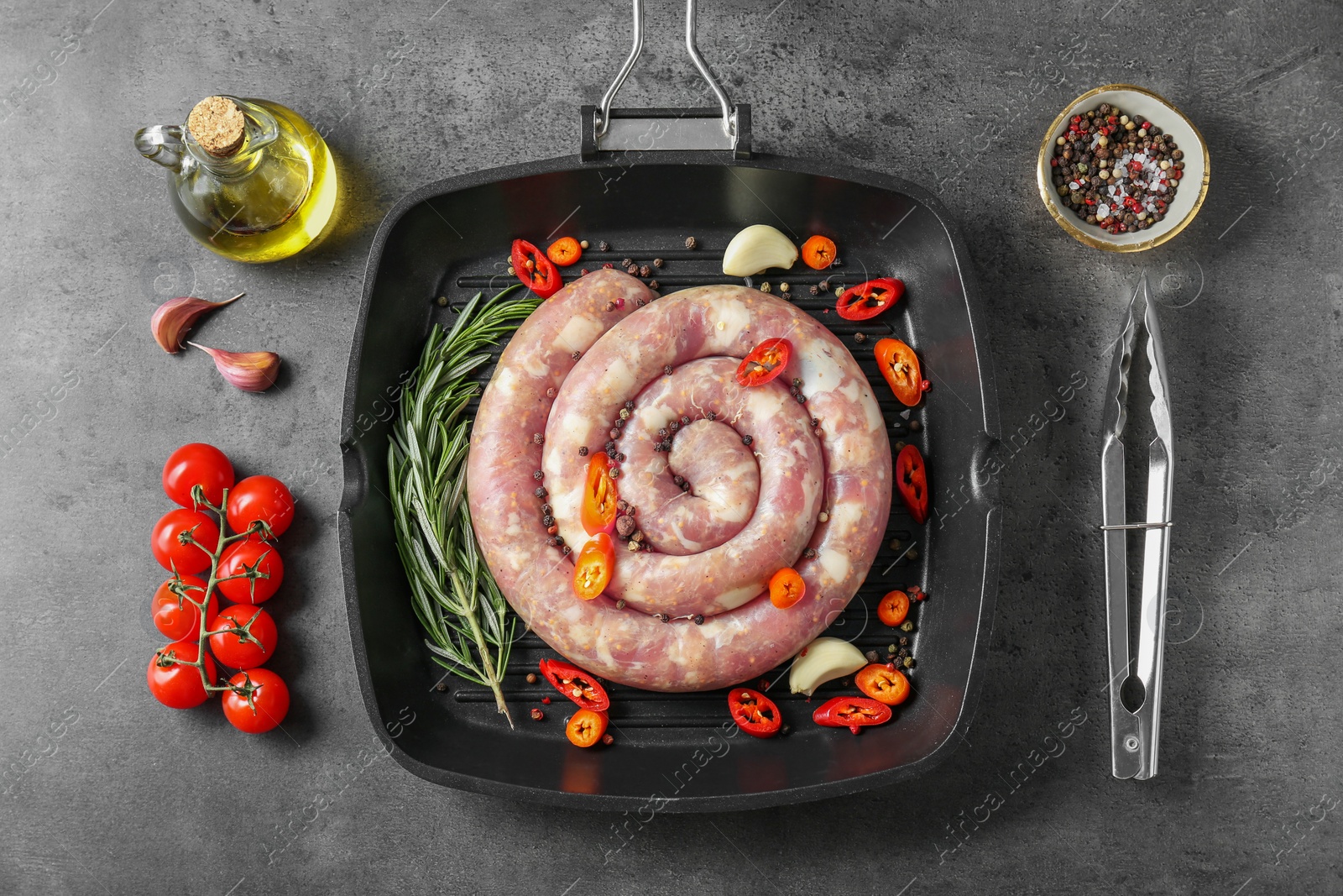 Photo of Pan with raw homemade sausage, spices, oil and tomatoes on grey table, flat lay