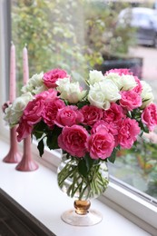 Vase with beautiful bouquet of roses and candles on windowsill indoors