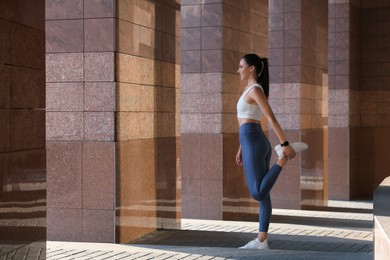 Beautiful woman in stylish sportswear stretching outdoors, space for text