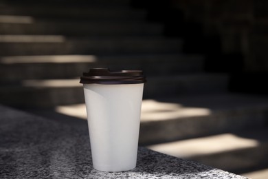 Takeaway cardboard coffee cup with plastic lid outdoors, space for text