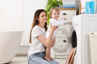 Mother with her daughter washing baby clothes in bathroom