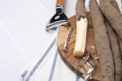Photo of Raw salsify roots and peeler on white tiled table, space for text