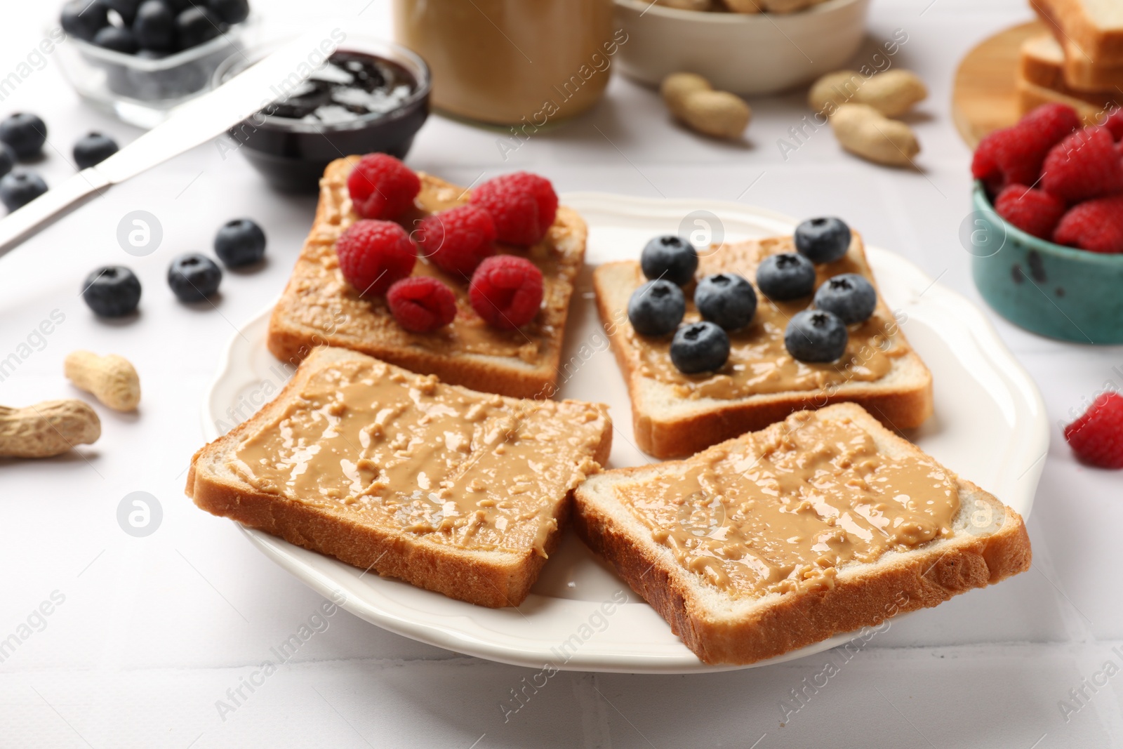 Photo of Delicious toasts with peanut butter, raspberries and blueberries on white table, closeup