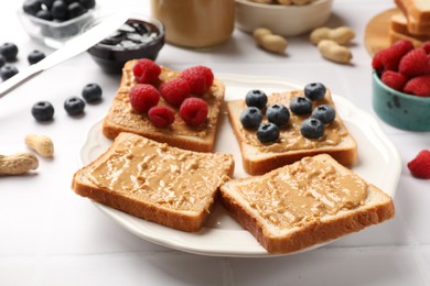 Photo of Delicious toasts with peanut butter, raspberries and blueberries on white table, closeup