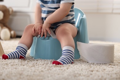 Photo of Little child sitting on plastic baby potty indoors, closeup