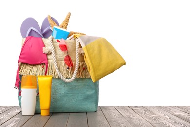 Stylish bag with beach accessories on wooden table against white background