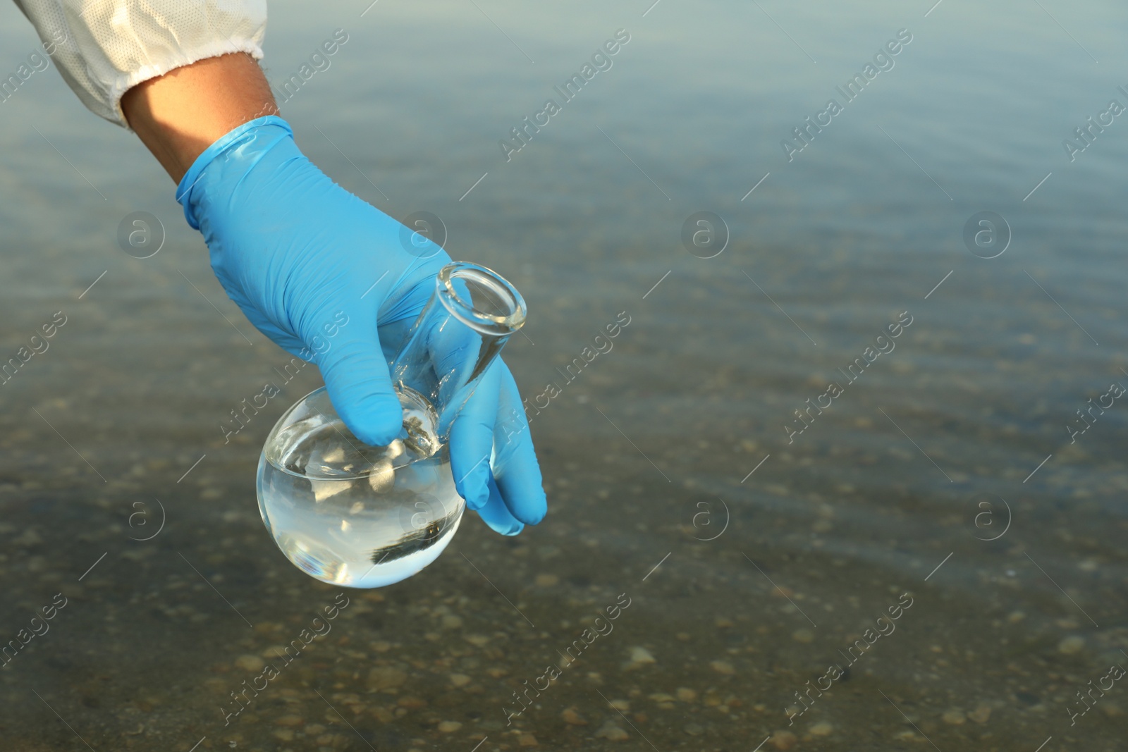 Photo of Scientist with florence flask taking sample from river for analysis, closeup