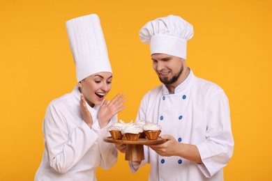 Photo of Happy professional confectioners in uniforms holding delicious cupcakes on yellow background