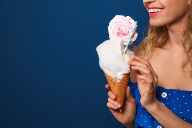 Photo of Young woman holding cotton candy dessert on blue background, closeup. Space for text
