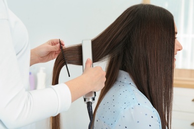 Photo of Hairdresser using modern flat iron to style client's hair in salon