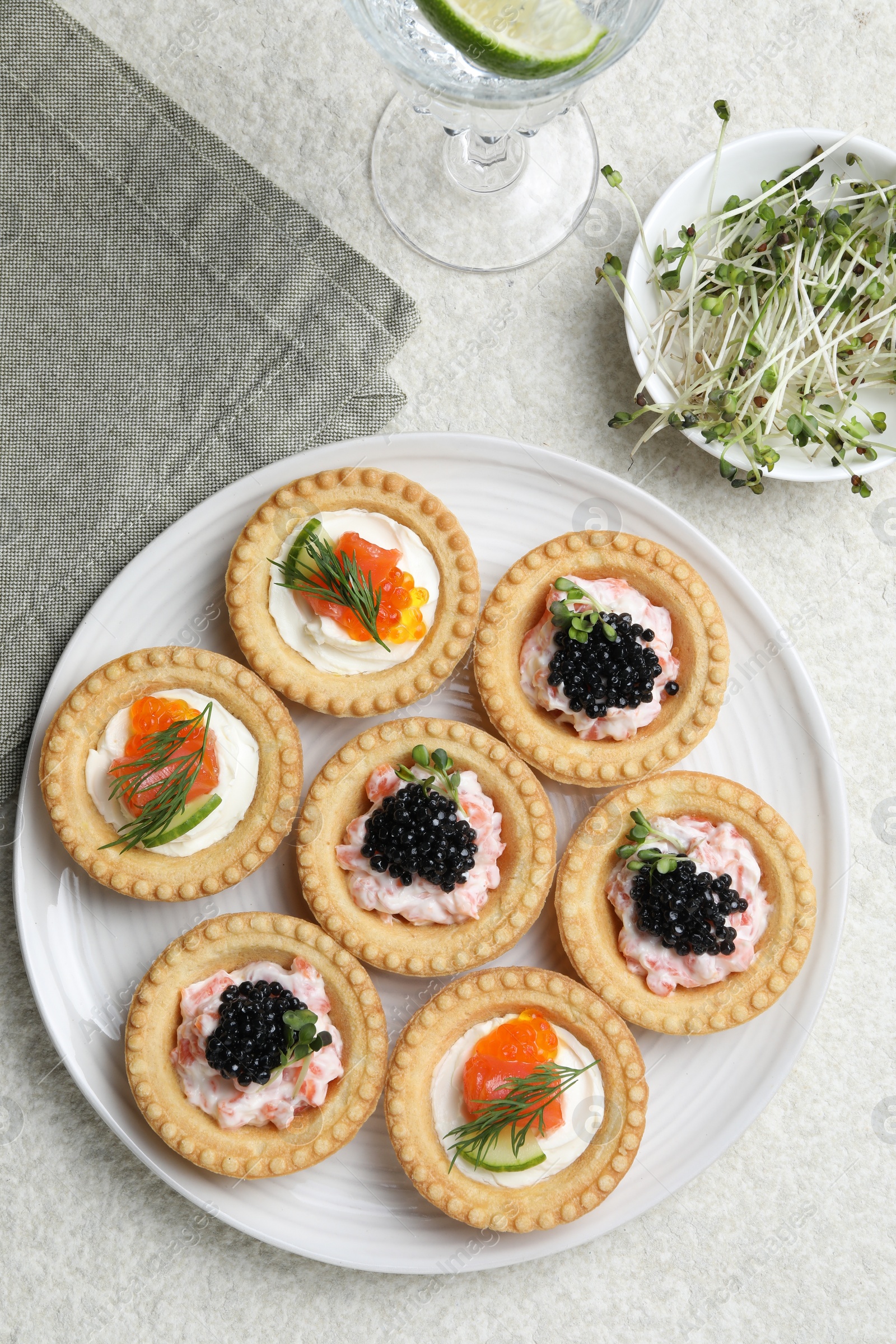 Photo of Delicious canapes with salmon, caviar, microgreens and glass of water on beige textured table, flat lay