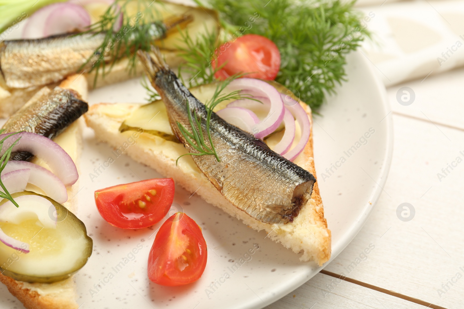 Delicious sandwiches with sprats, pickled cucumber, onion and dill served on white wooden table, closeup Photo of Delicious sandwiches with sprats, pickled cucumber, onion and dill served on white wooden table, closeup