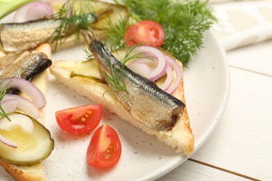 Photo of Delicious sandwiches with sprats, pickled cucumber, onion and dill served on white wooden table, closeup